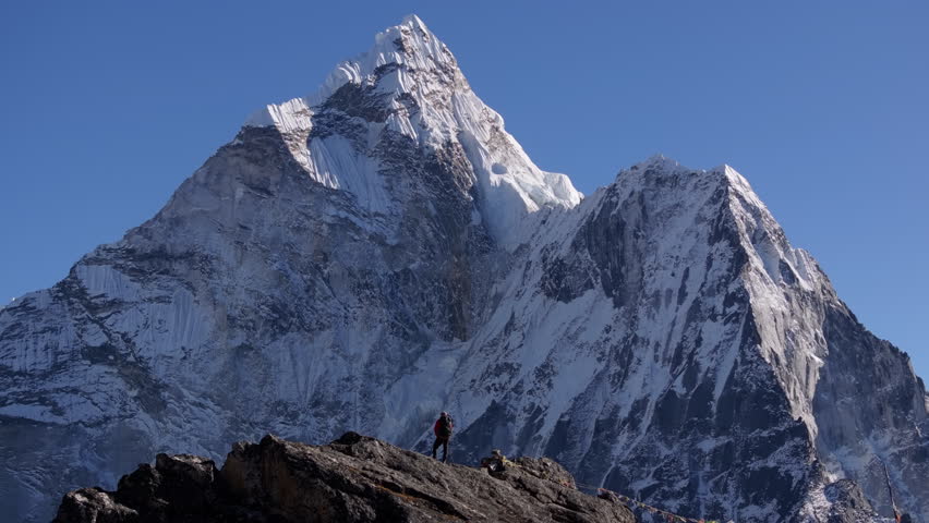 Mountaineer stands atop Nangkartshang Peak, silhouetted against massive Mount Everest, showcasing majestic Himalayan landscape and Nepalese wilderness