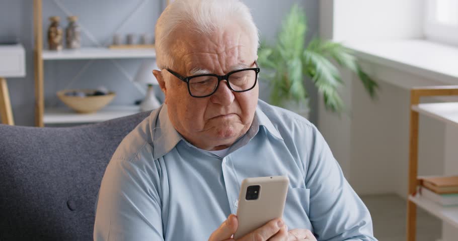 Elderly man has bad eyesight, puts off eyeglasses and focused in smartphone screen, tries to read received message, cannot understand how to use app, has some problems. Technology annd retirement