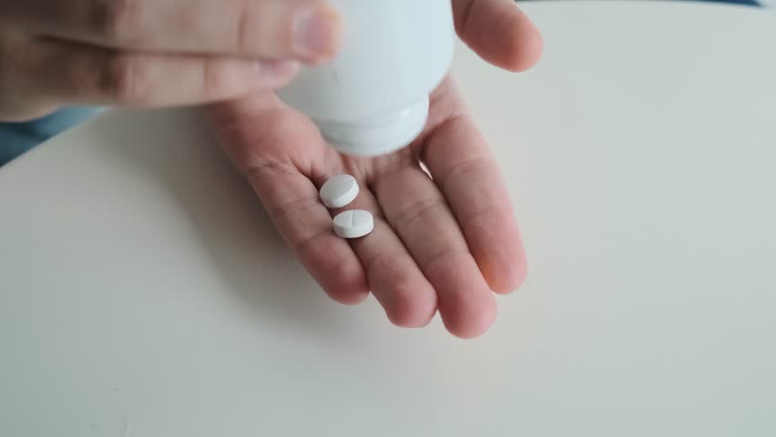 Man pouring painkiller white tablets in male hand from medicine bottle. Palm of medical specialist with antibiotics for recovery, treatment and supplementation. Health support and treatment