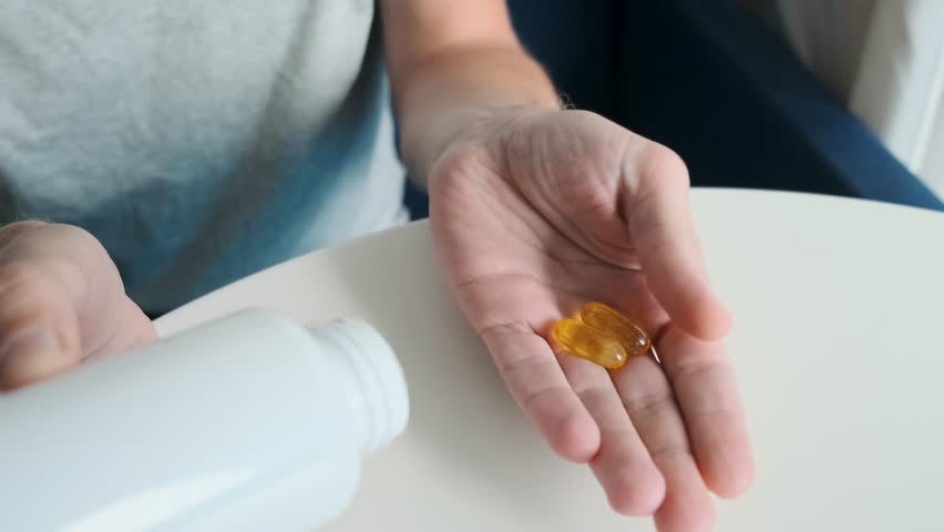 Man hand holding two soft gel capsules with fish oil, omega3 and vitaminD supplements with pill bottle. Nutritional supplement. Health support and treatment concept. Top view
