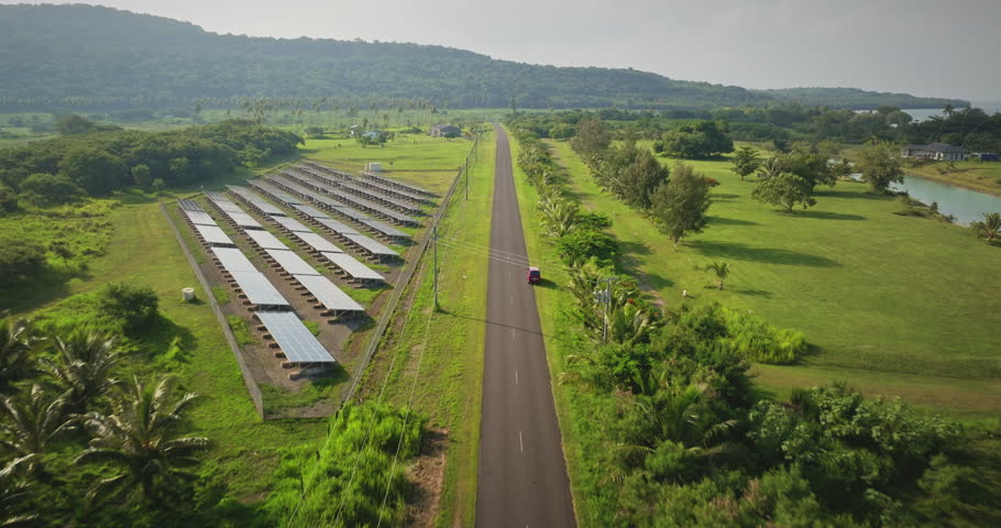 Vanuatu, Port Villa: solar electric panels along the road, surrounded by green fields and distant hills on Efate Island. Sustainable energy wild nature landscape. Aerial view drone flight footage
