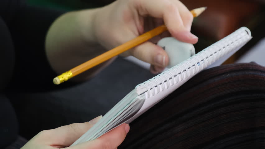Artist sketches with pencil in spiral-bound notebook and erases imperfections with white eraser. Process of drawing with corrections in art studio
