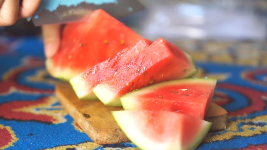 A close-up of hands slicing a juicy red watermelon on a wooden cutting board, highlighting the freshness and summer feel.