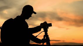 Photographer with backpack takes beautiful sunset with camera and tripod. Traveler with tripod, camera takes beautiful pictures of landscape of sunny sky with clouds. Tourist photographer, nature sky - Powered by Shutterstock - Get 15% off with code: PIKWIZARD15