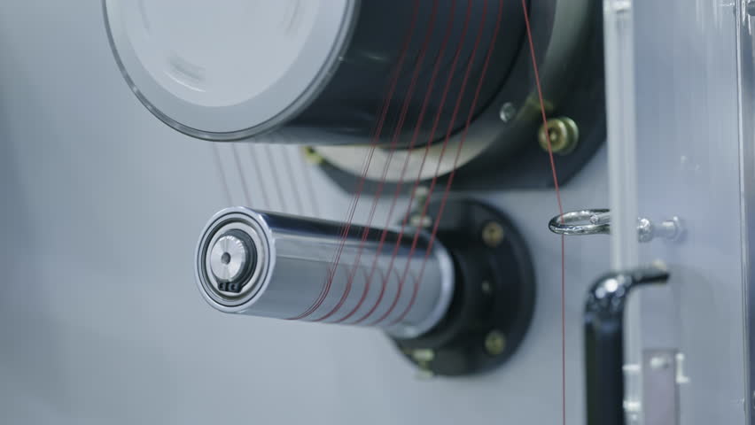Detailed view of red threads running through a precision winding machine in textile manufacturing. Modern equipment for high-speed thread or fiber processing.