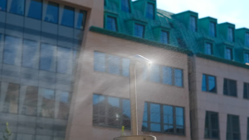 Street cooling system spraying water mist on a hot day. Refreshing water mist spraying from a street cooling system, providing relief from the summer heat in a city setting