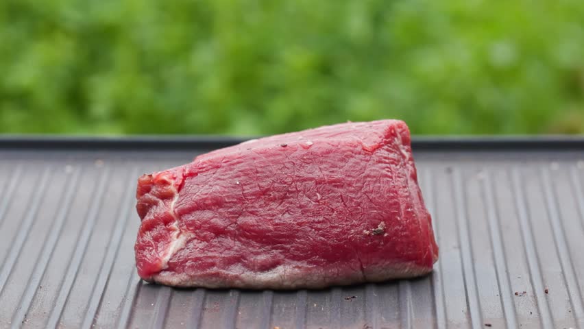 outdoor cooking. cook preparing fresh raw beef fillet mignon steak with oil and spices on hot grill pan for making delicious meal in garden, food closeup, outdoors natural light