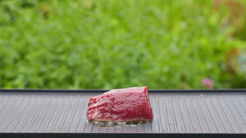 outdoor cooking. cook preparing fresh raw beef fillet mignon steak with oil and spices on hot grill pan for making delicious meal in garden, food closeup, outdoors natural light