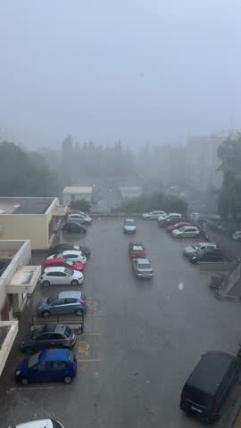 Heavy rainfall drenching deserted parking lot in Split, Croatia, revealing hurricane aftermath with misty, gray atmosphere and water-covered urban landscape surrounding parked vehicles