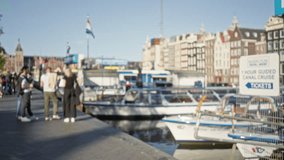 People blurred on amsterdam canal promenade with flags, boats, and historic buildings in background on a sunny day. - Powered by Shutterstock - Get 15% off with code: PIKWIZARD15