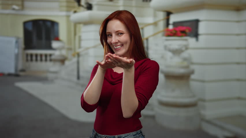 Woman smiling and making money gesture outdoors in urban city street, showcasing joy and confidence in a casual outfit.