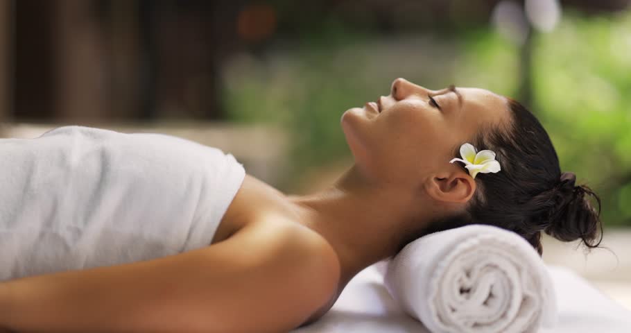 Side profile of a beautiful tanned woman wrapped in a towel and lying in a tropical spa setting. Ideal for wellness, aromatherapy, and luxury resort promotional content in slow motion.