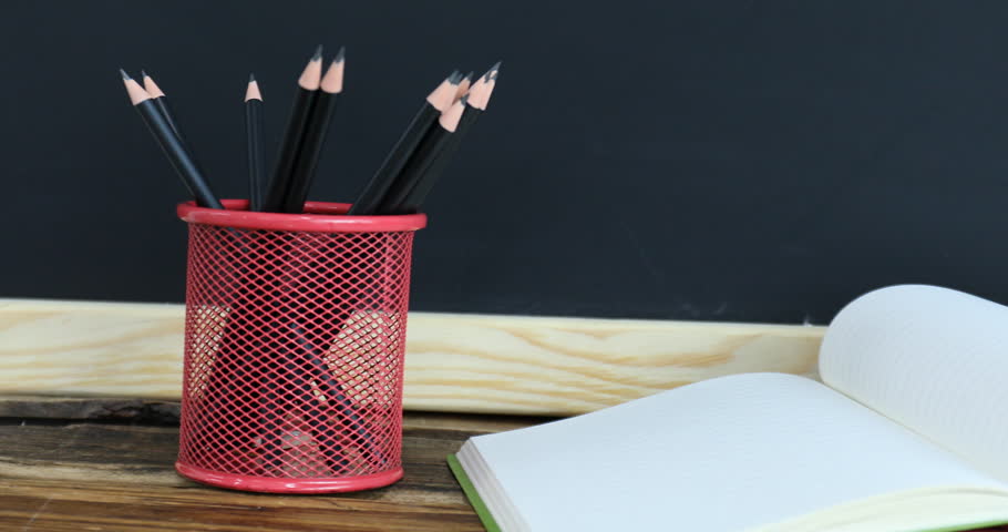 Different stationery and apple on wooden table near blackboard, closeup. Camera moving right
