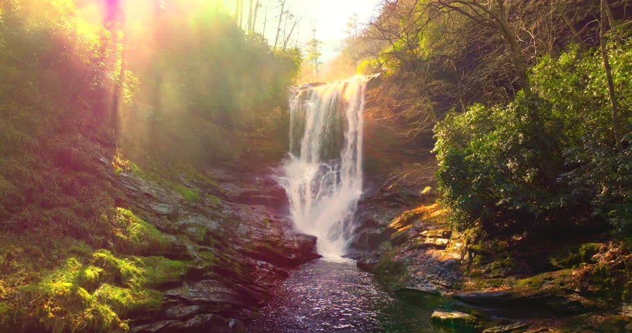Autumn colored woods around Dry Falls in North Carolina. Scenic waterfall with natural walkway behind rushing water and forest in full fall bloom
