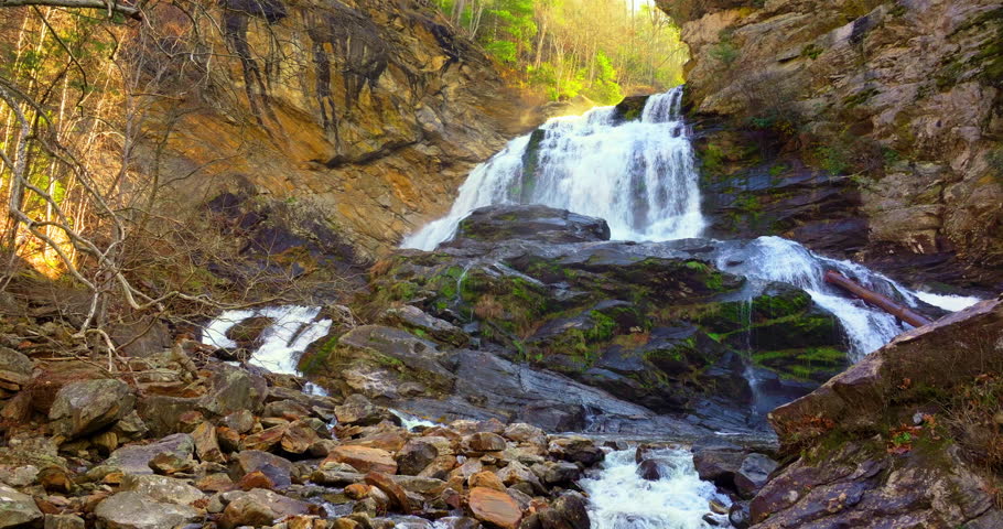 Large mountain waterfall. Aerial view of Cullasaja Falls in autumn, with clear water crashing through a rugged landscape of vibrant red and yellow forest
