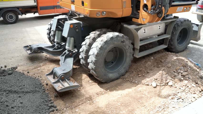 Close-Up of Excavator Lowering Stabilizer Legs for Stability at Highway Construction Site