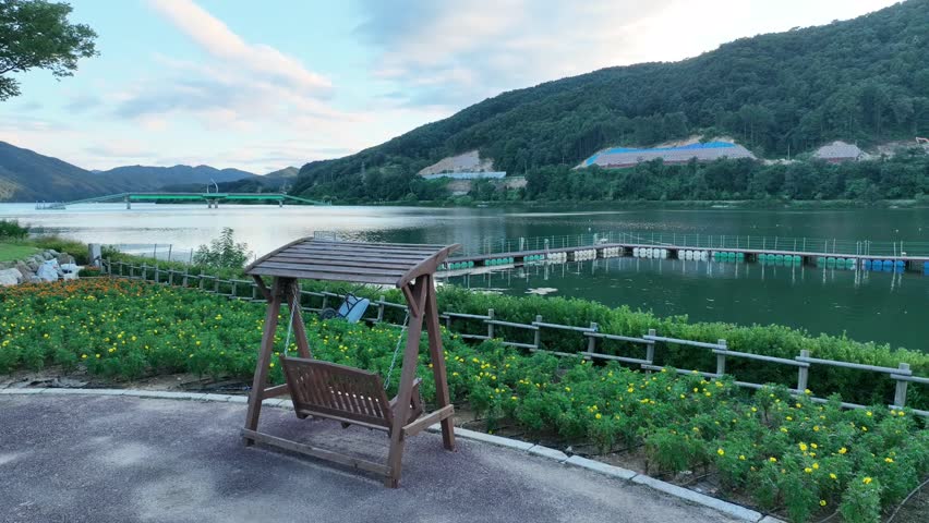 Wooden swing bench facing tranquil lake with floating dock and wildflowers in scenic park
