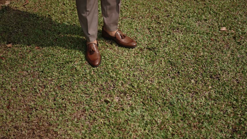 elegant brown dress shoes and formal trousers stride over trimmed lawn during outdoor event