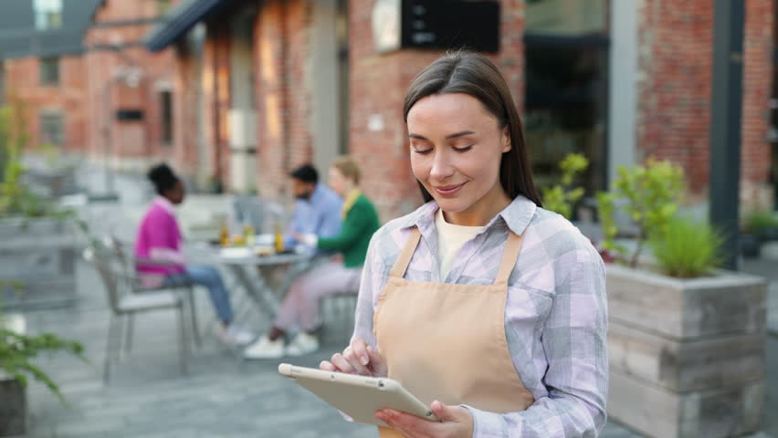 A smiling waitress takes an order on a tablet at an outdoor restaurant. - Powered by Shutterstock - Get 15% off with code: PIKWIZARD15