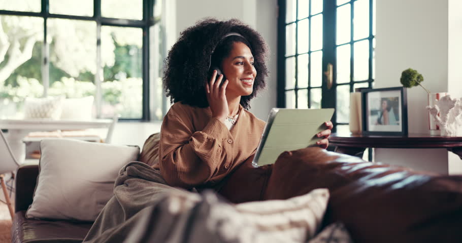 Headphones, tablet and happy woman in living room for music, streaming podcast or scroll app. Radio, technology and African person relax in home for online audio, sound and listening to audiobook