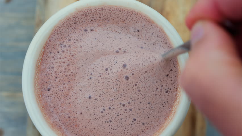 Close up of a hand mixing into a a cup of hot chocolate with a spoon