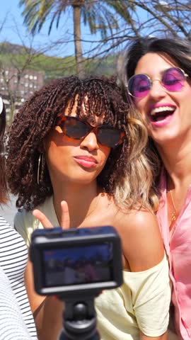 Close female friends capturing travel memories during sunny summer vacation, recording dynamic vlog content while exploring urban destination together with authentic joy and enthusiasm