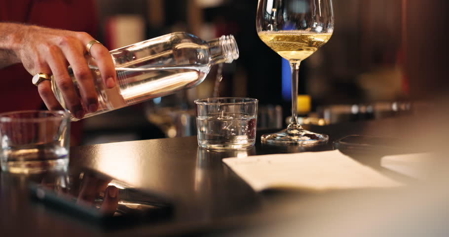 Pouring, water and wine with hand of bartender in restaurant for hospitality, refreshment or service. Alcohol, bottle and nightlife with person at counter in pub for beverage or drinks order closeup