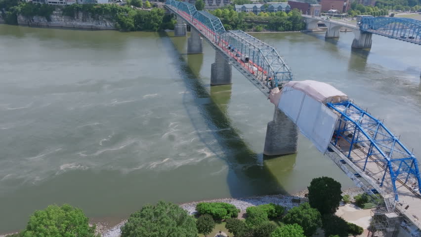An aerial view of Chattanooga’s Walnut Street Bridge shows it partially covered for maintenance, spanning the Tennessee River with shadows stretching across the water below.
