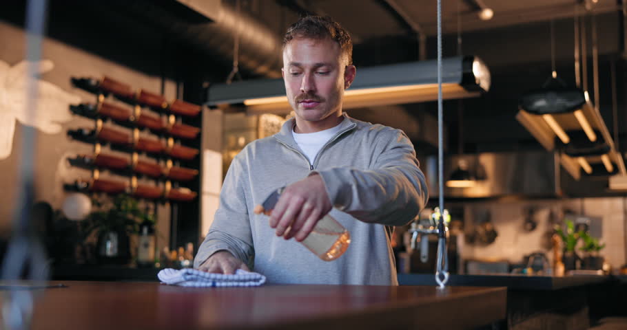 Restaurant, man and cleaning counter with spray for hygiene, disinfection or bacteria removal. Small business, manager or cloth to wipe surface for wine bar maintenance, safety policy or work routine