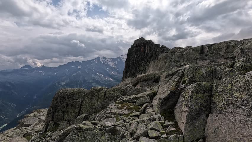 Jagged alpine ridge with large boulders and a moody sky overlooking the Monte Rosa range in Italy.
