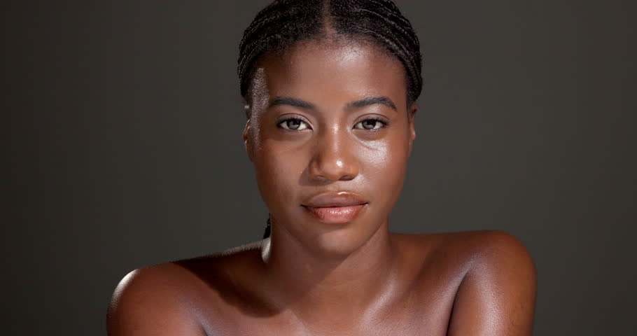 Face, confident and woman with glow, studio or bodycare with cosmetics, healthy skin or dermatology. Gray background, black person and pride for shine, soft and self care with treatment and wellness