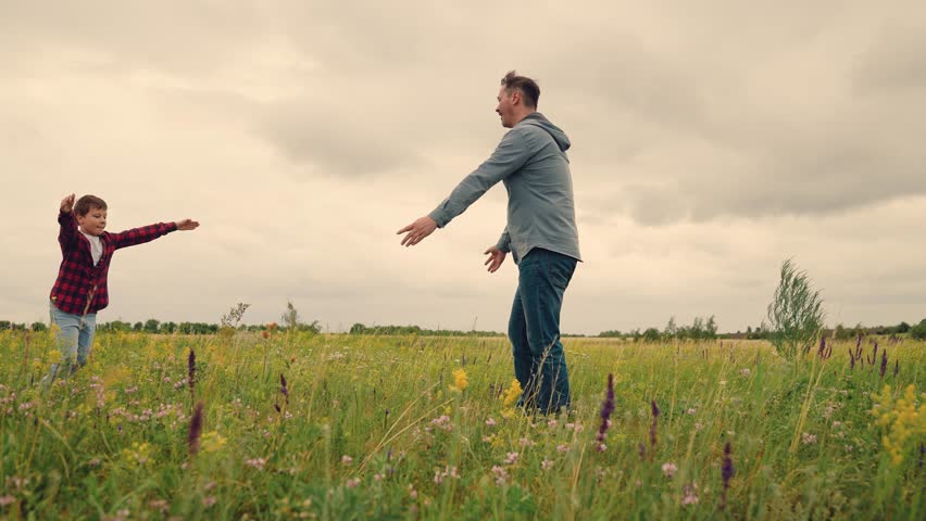 Dad swings son in open field, boy imagines flying high, parent and child create memories, outdoor family happiness, playing superhero together, smiling faces in wildflower meadow, endless summer joy