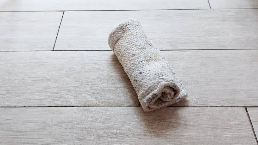 A hand gently unfolds a soft floor rag on sunlit tiles. Light catches its texture as quick motions signal a tidy rhythm-an everyday gesture of comfort and ease
