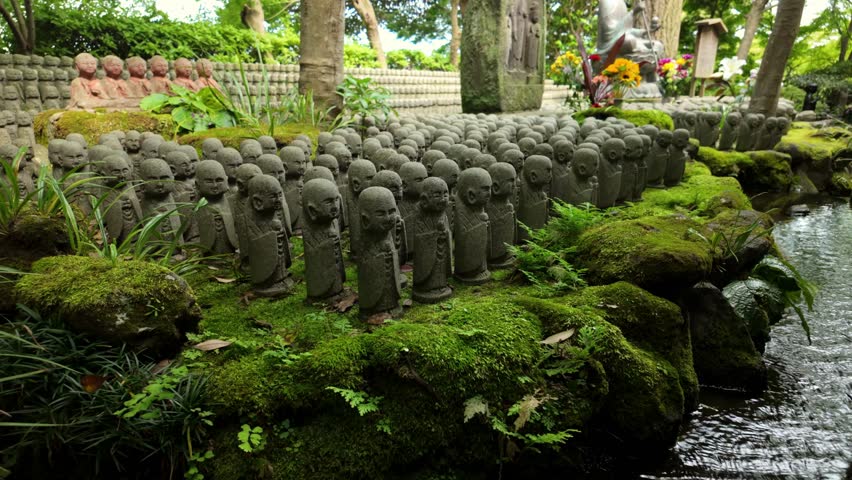 Static shot of hundreds of small stone Jizo statues lined along a moss-covered pond in a peaceful temple garden at Hasedera in Kamakura, Japan