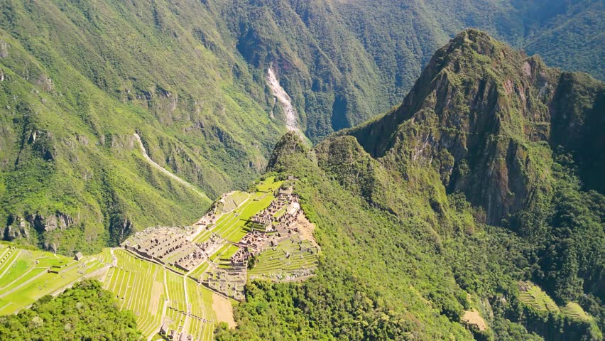 Drone orbits above Machu Picchu with sunlight cutting through misty mountain air at dawn, establishing