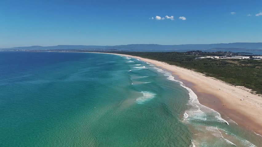 Aerial establishing dolly of long beach and open ocean horizon at Port Kembla with waves and clean shoreline, Sydney NSW Australia