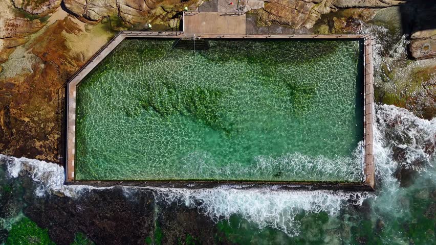 Aerial rock pool surrounded by ocean waves in Cronulla near rocky headland, Sydney NSW Australia