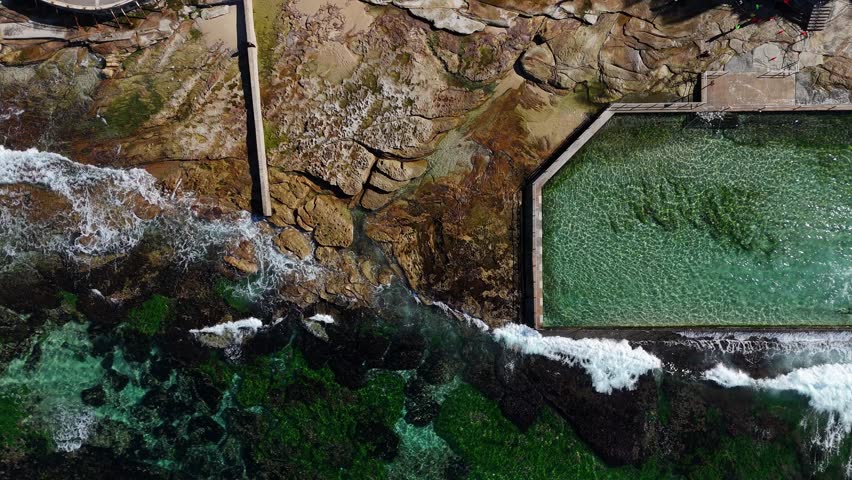 Aerial top down of rock pool surrounded by waves and rocky shoreline in Cronulla, Sydney NSW Australia