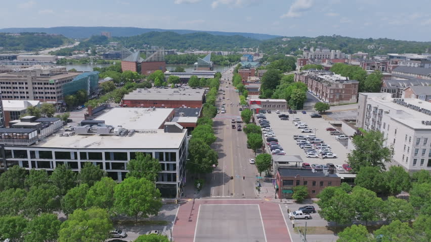 An aerial view of Market Street in downtown Chattanooga, TN, looking north toward the Tennessee Aquarium and Walnut Street Bridge, with the river and surrounding hills in the distance.