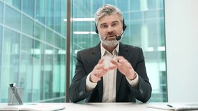 Webcam view. Confident businessman in headset talking on video call looking at camera sitting in office. Mature entrepreneur has business meeting. Manager in suit speaks remotely at online conference - Powered by Shutterstock - Get 15% off with code: PIKWIZARD15