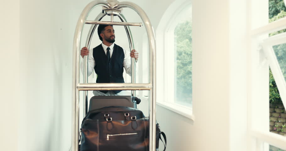 Man, hotel and hospitality with luggage trolley, push and bag delivery for client at job in hallway at luxury lodge. Person, cart and support for guest baggage, concierge and accommodation at resort