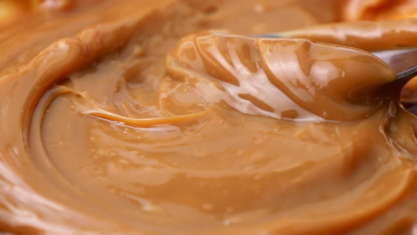 Sweet brown caramel toffee sauce spreading with a spoon close up