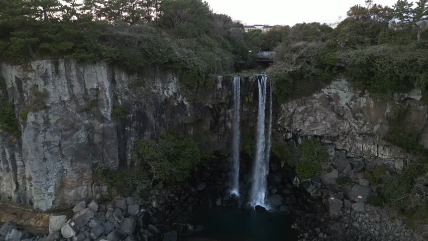 Drone aerial view in South Korea flying in front of a waterfall over the sea rocky area jeju island