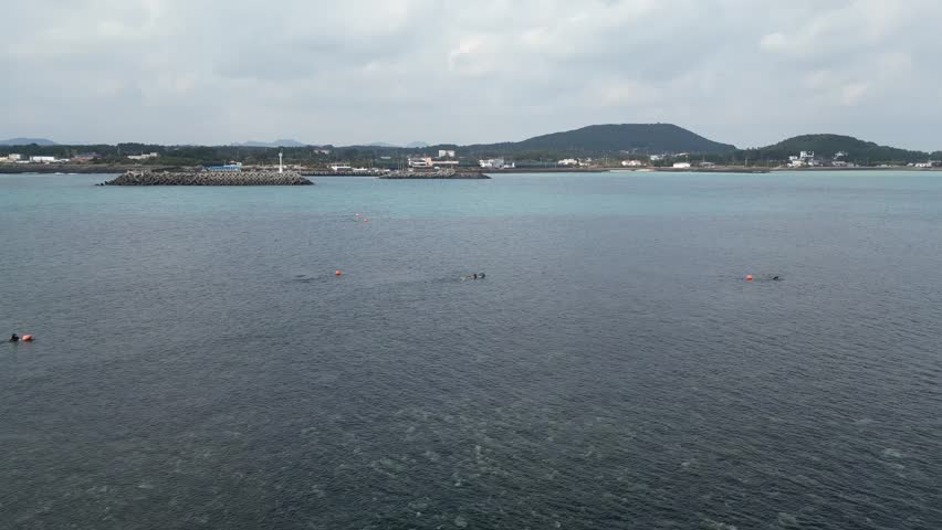 Drone aerial view in South Korea countryside flying over the sea with green island rocky shallow area haenyeo women divers fishing jeju island cloudy