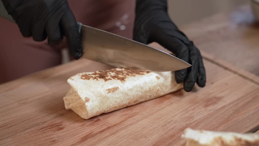 Hands of Female Chef that creates Homemade Burrito in Kitchen, Cutting tortilla and Shows meat and vegetables inside.