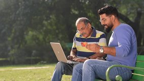 Young indian man showing bank card and laptop how to uses to his father at park - Powered by Shutterstock - Get 15% off with code: PIKWIZARD15