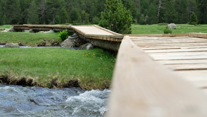 Winding Wooden Bridge-trail over Mountain Streams on Green Meadow. Alpine Landscape in "Aigüestortes i Estany de Sant Maurici National Park". Catalan Pyrenees, Spain. Ideal for Hiking and Tourism.
