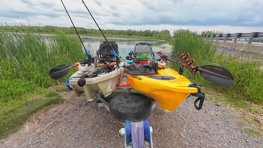 Fishing kayaks prepared for the launch and fishing at the lake. Boat trailer at the ramp water access attached to the truck hitch mount and fishing pedal kayaks. Sport fish tournament at spring.