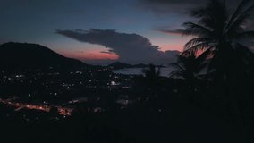 Palm trees frame breathtaking sunset over coastal cityscape in southeast asia, casting warm glow over landscape as night descends. Night city lights under palm silhouette. Nightlife on island - Powered by Shutterstock - Get 15% off with code: PIKWIZARD15