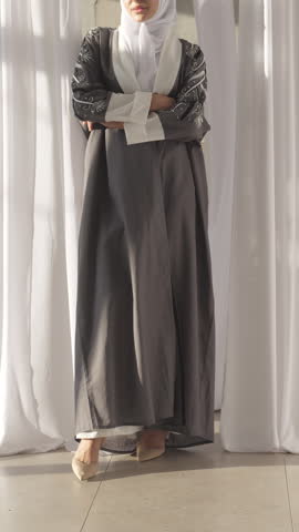 Muslim woman walks presenting grey linen Abaya paired with chiffon hijab. Lady shows traditional outfit with rhinestone embroidery on sleeves